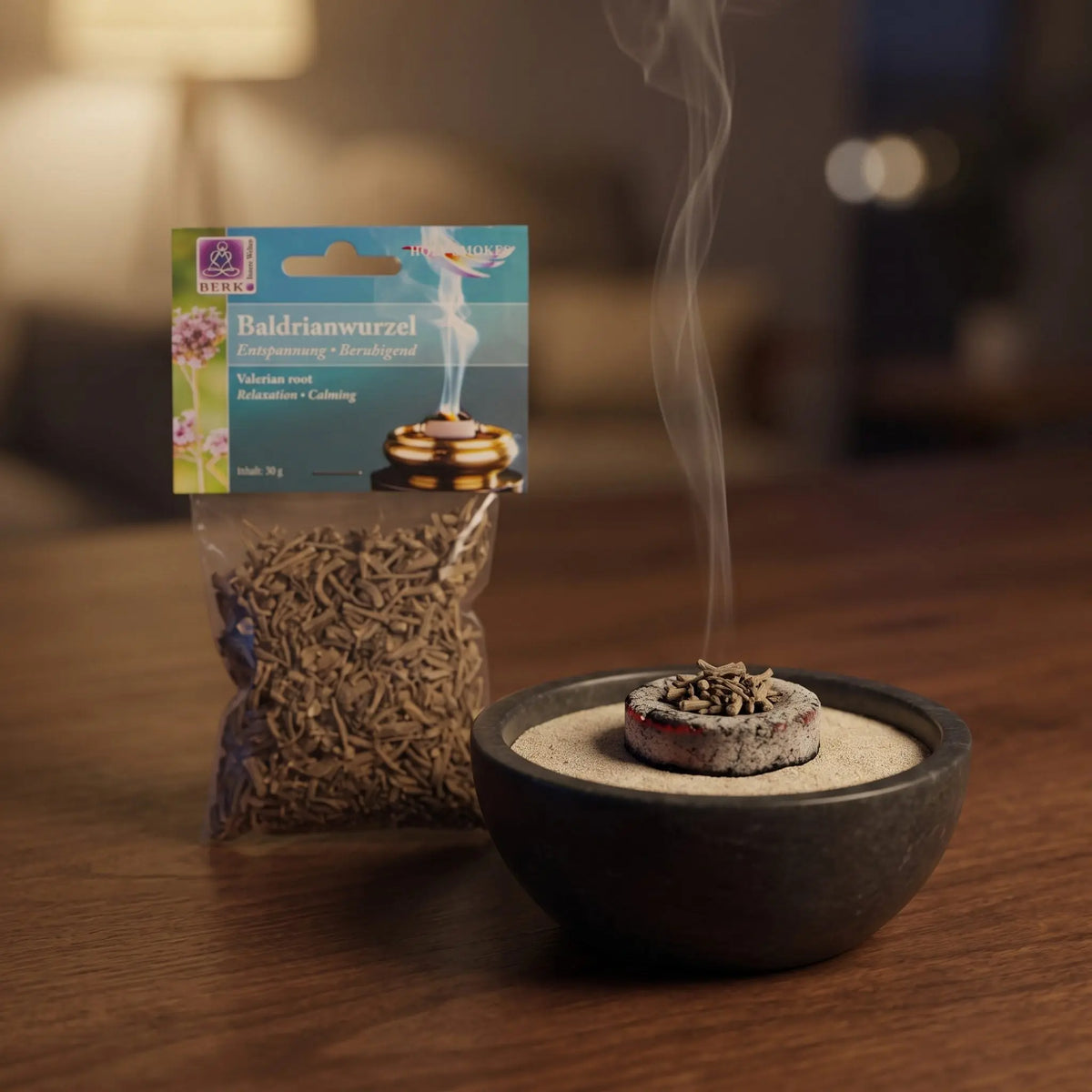 Baldrianwurzel, sortenreines Räucherwerk von Berk, 30 g: eine Prise Baldrianwurzel glimmt auf der Räucherkohle, dahinter die Tüte, feiner Rauch steigt auf einer dunklen Holzplatte am Abend auf – Spirit of Gaia