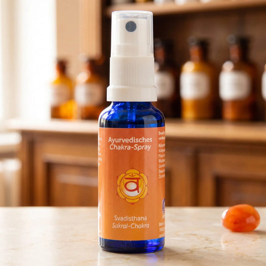 Ayurvedisches Chakra-Spray Svadisthana (Sakral-Chakra): 30-ml-Sprühflasche aus blauem Glas auf Marmortheke vor Apothekerschrank, daneben Karneol – Spirit of Gaia
