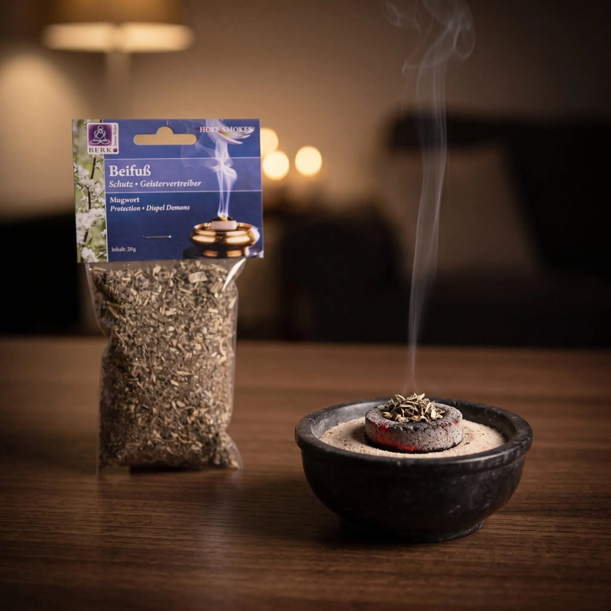 Beifußkraut, sortenreines Räucherwerk von Berk, 20 g: eine Prise Beifuß glimmt auf der Räucherkohle, dahinter die Tüte, feiner Rauch steigt auf einer dunklen Holzplatte am Abend auf – Spirit of Gaia