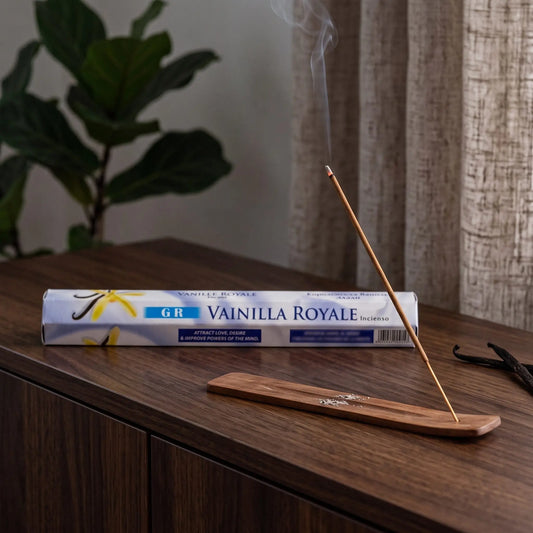 GR Royal Vanilla Räucherstäbchen: glimmendes Räucherstäbchen mit feinem Rauch im Holzhalter, dahinter die Sechseck-Packung, auf einem Sideboard am Abend