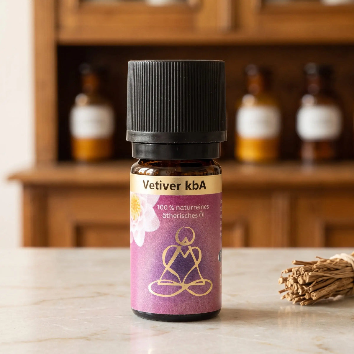 Ätherisches Öl Vetiver: Fläschchen aus Braunglas auf Marmortheke vor Apothekerschrank, daneben Vetiverwurzeln – Spirit of Gaia