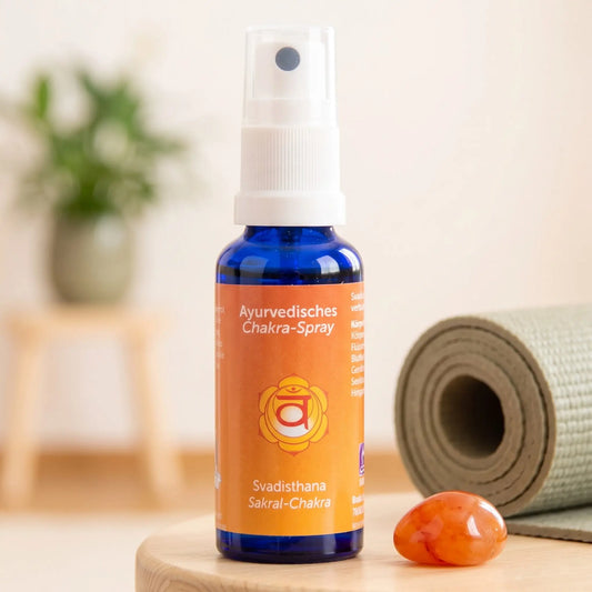 Ayurvedisches Chakra-Spray Svadisthana (Sakral-Chakra): 30-ml-Sprühflasche auf einem Holzhocker neben einer gerollten Yogamatte, daneben Karneol