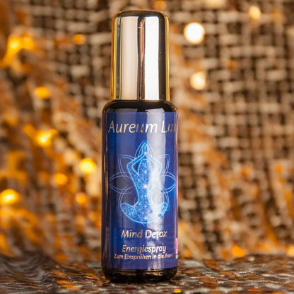 Energiespray Aureum Lux Mind Detox, 50-ml-Sprühflasche aus Violettglas vor glitzerndem Hintergrund