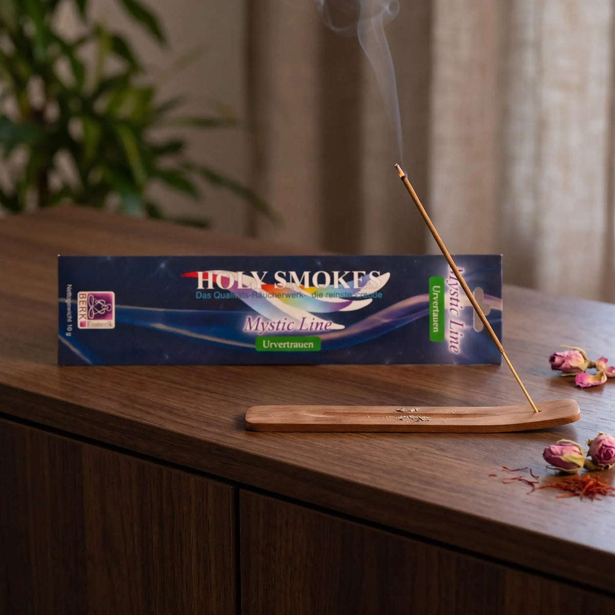 Urvertrauen Räucherstäbchen Holy Smokes Mystic Line: glimmendes Räucherstäbchen mit feinem Rauch im Holzhalter, dahinter die Packung, auf einem Sideboard am Abend