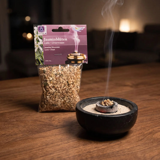 Jasminblüten, sortenreines Räucherwerk von Berk, 10 g: eine Prise Jasminblüten glimmt auf der Räucherkohle, dahinter die Tüte, feiner Rauch steigt auf einer dunklen Holzplatte am Abend auf – Spirit of Gaia