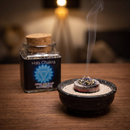 Halschakra, Chakra-Räuchermischung von Berk, 50 ml im Korkglas: glimmende Räucherkohle mit einer Prise der grau-blauen Mischung in einer Specksteinschale, dahinter das Korkglas, feiner Rauch steigt auf einer dunklen Holzplatte am Abend auf – Spirit of Gaia