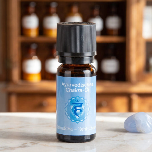 Ayurvedisches Chakra-Öl Vishuddha (Kehl-Chakra): 10-ml-Fläschchen aus Braunglas auf Marmortheke vor Apothekerschrank, daneben blauer Chalcedon – Spirit of Gaia