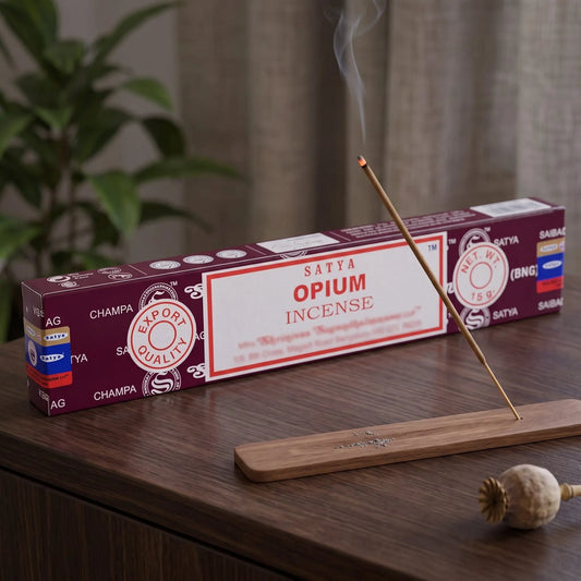 Satya Opium Räucherstäbchen: glimmendes Räucherstäbchen mit feinem Rauch im Holzhalter, dahinter die Packung, auf einem Sideboard am Abend