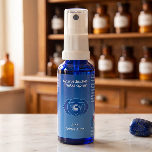 Ayurvedisches Chakra-Spray Ajna (Stirn-Chakra): 30-ml-Sprühflasche aus blauem Glas auf Marmortheke vor Apothekerschrank, daneben Lapislazuli – Spirit of Gaia