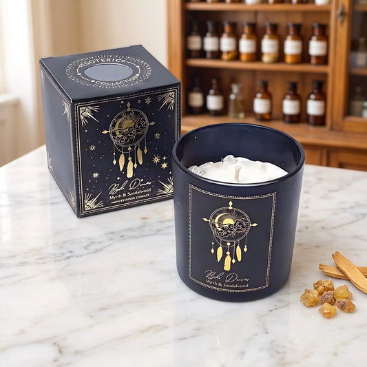 Manifestationskerze Boho Dreams mit Bergkristall (Myrrhe & Sandelholz) von Pure Works: Kerze im schwarzen Glas und schwarze Schachtel mit Goldprägung auf Marmortheke vor Apothekerschrank, daneben Myrrheharz und Sandelholzspäne – Spirit of Gaia