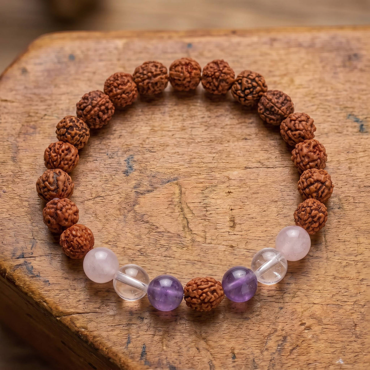 Draufsicht auf das Rudraksha Armband mit Edelsteinen auf altem Holz: Rosenquarz, Bergkristall und Amethyst um einen Rudraksha-Samen