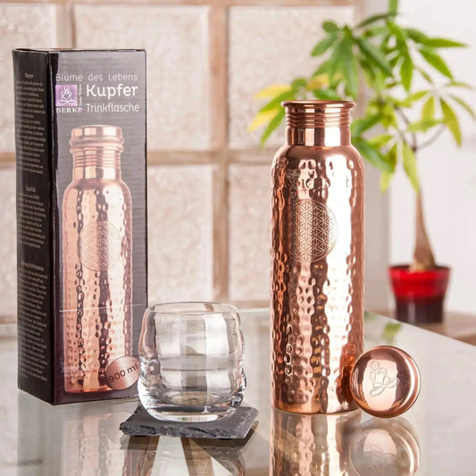 Handgehämmerte Kupfer-Trinkflasche mit 900 ml Fassungsvermögen, eingravierter Blume des Lebens und sicherem Schraubverschluss, auf einem Glastisch.