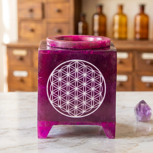 Aromalampe Blume des Lebens: violetter Speckstein mit gravierter Blume des Lebens auf Marmortheke vor Apothekerschrank, daneben ein Amethyst – Spirit of Gaia