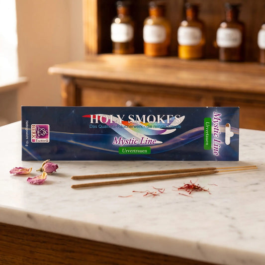 Urvertrauen Räucherstäbchen Holy Smokes Mystic Line: Packung auf einer Marmortheke vor einem Apothekerschrank, davor zwei lose Räucherstäbchen, getrocknete Rosenknospen und Safranfäden – Spirit of Gaia