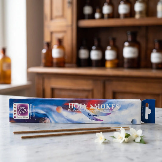 Jasmin Räucherstäbchen Blue Line: Packung auf einer Marmortheke vor einem Apothekerschrank, daneben zwei lose Räucherstäbchen und ein paar weiße Jasminblüten – Spirit of Gaia