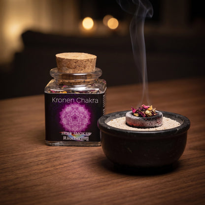 Kronenchakra, Chakra-Räuchermischung von Berk, 50 ml im Korkglas: glimmende Räucherkohle mit einer Prise der violetten Rosenmischung in einer Specksteinschale, dahinter das Korkglas, feiner Rauch steigt auf einer dunklen Holzplatte am Abend auf – Spirit of Gaia