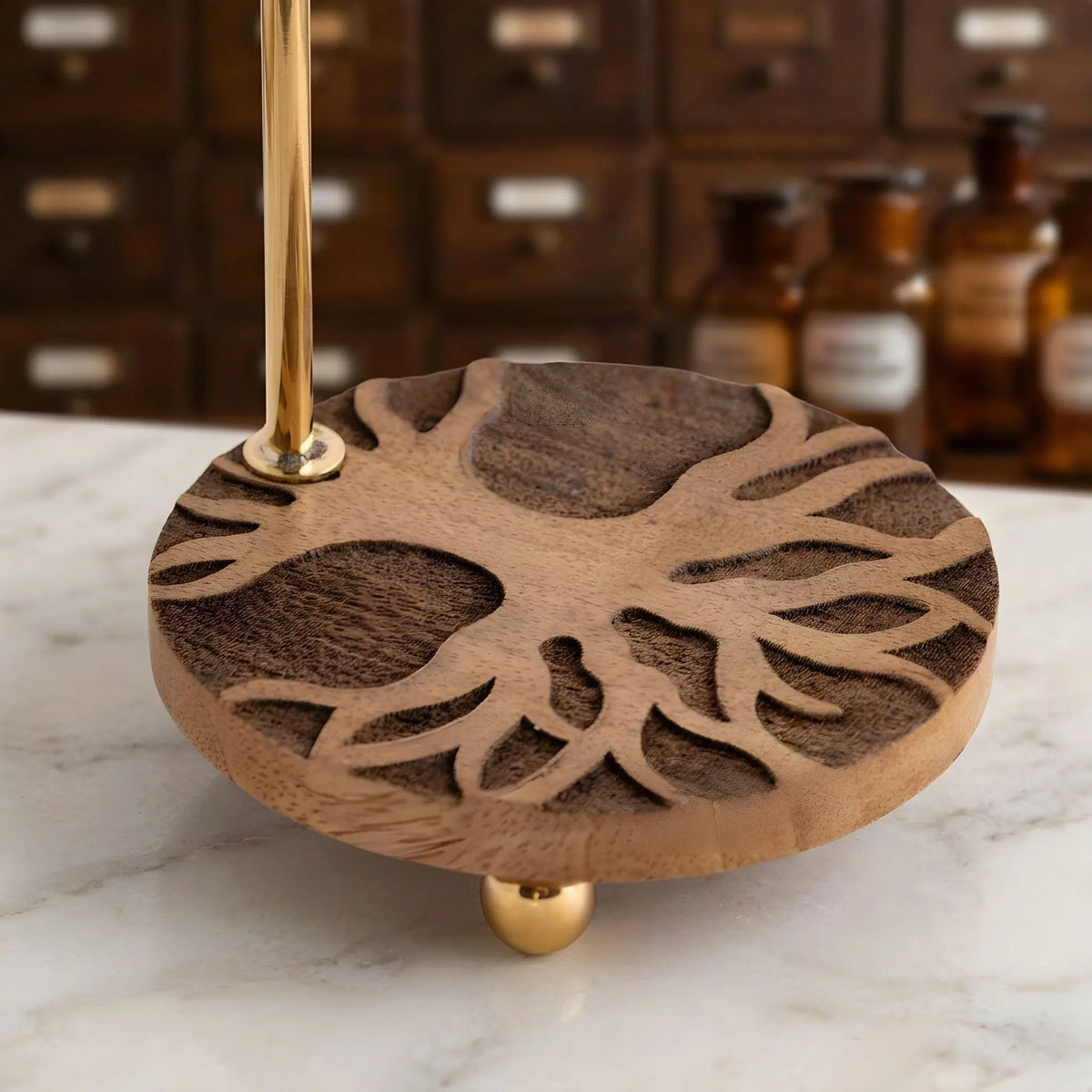 Der in den Mangoholzsockel geschnitzte Baum des Lebens aus der Nähe, dahinter unscharf der Apothekerschrank