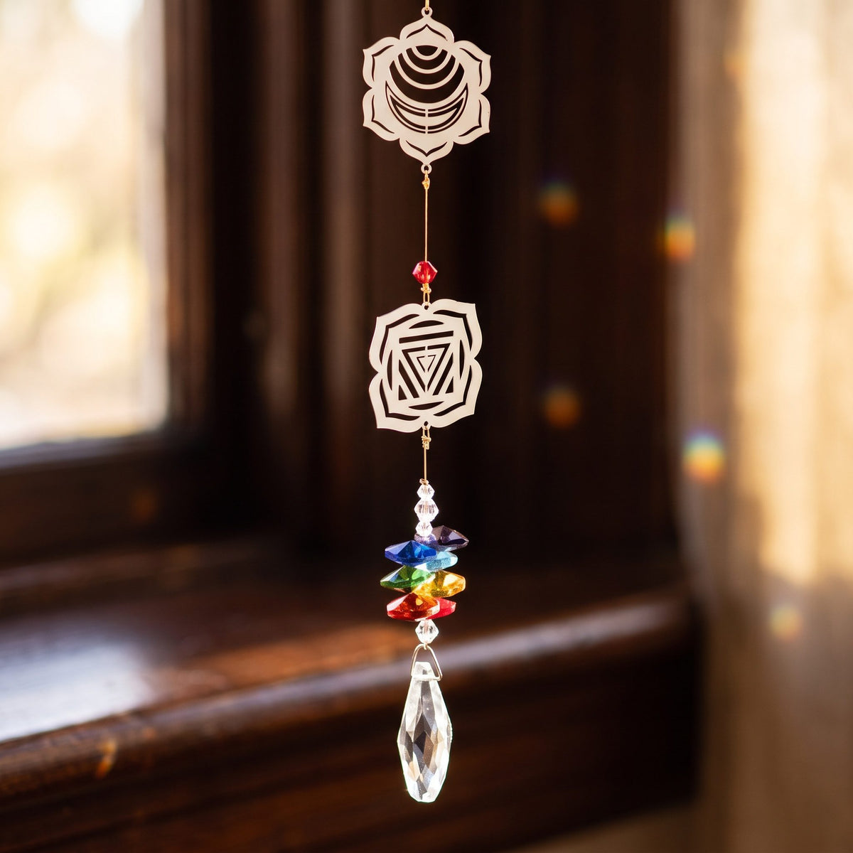Nahaufnahme der unteren Chakra-Symbole mit Stapel farbiger Glasplättchen und klarem Glastropfen vor unscharfem Fenster
