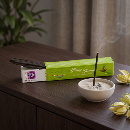 Ylang Ylang Räucherstäbchen naturrein, Holy Smokes Green Line: glimmendes Räucherstäbchen in einer Keramikschale mit Sand, dahinter die geöffnete Packung, auf einem Sideboard am Abend