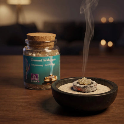 Gummi Arabicum, reines Räucherharz von Berk, 60 ml im Korkglas: einige helle Gummi-Arabicum-Stücke glimmen auf der Räucherkohle, dahinter das Korkglas, feiner Rauch steigt auf einer dunklen Holzplatte am Abend auf – Spirit of Gaia