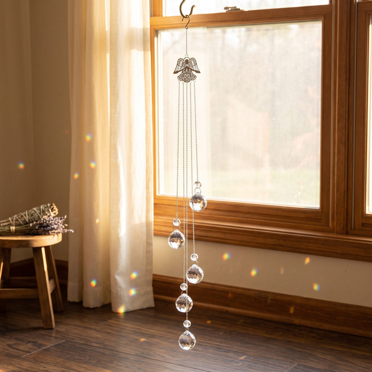 Engel Suncatcher am hohen Fenster mit Vorhang, Lichtpunkte in Regenbogenfarben auf dem Holzboden