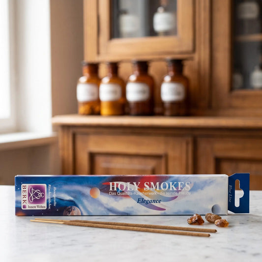 Elegance Räucherstäbchen Blue Line: Packung auf einer Marmortheke vor einem Apothekerschrank, daneben zwei lose Räucherstäbchen und ein paar Stücke Bernsteinharz – Spirit of Gaia