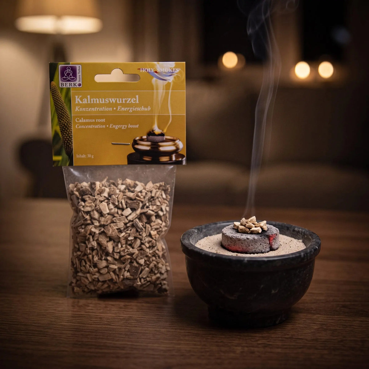 Kalmuswurzel, sortenreines Räucherwerk von Berk, 30 g: einige Stücke Kalmuswurzel glimmen auf der Räucherkohle, dahinter die Tüte, feiner Rauch steigt auf einer dunklen Holzplatte am Abend auf – Spirit of Gaia