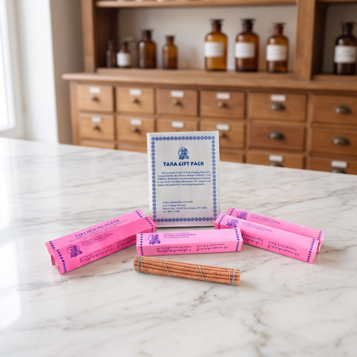 Tara Healing Incense: silberne Tara Gift Pack Box mit vier rosa Päckchen und einem offenen Stäbchenbündel auf einer Marmortheke vor einem Apothekerschrank