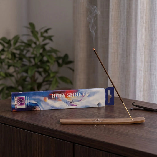 Vanille Räucherstäbchen Holy Smokes Blue Line: glimmendes Räucherstäbchen mit feinem Rauch im Holzhalter, dahinter die Packung, auf einem Sideboard am Abend
