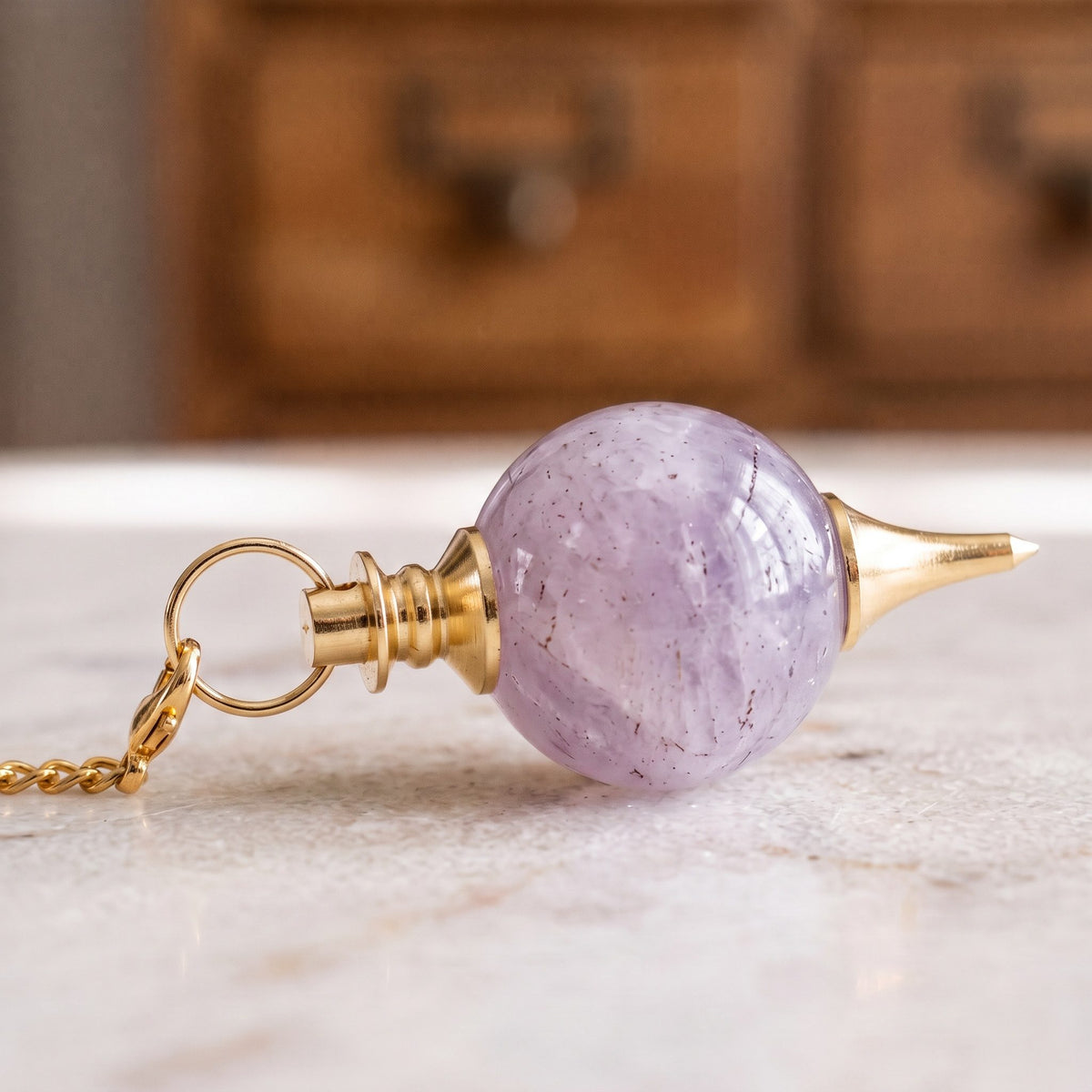 Nahaufnahme der violetten Amethystkugel mit gestufter Messingkappe und Messingspitze, liegend auf Marmor