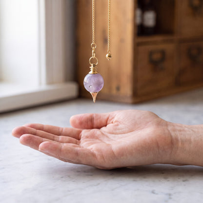 Das Amethyst-Pendel hängt ruhig an seiner Kette über einer offenen Handfläche