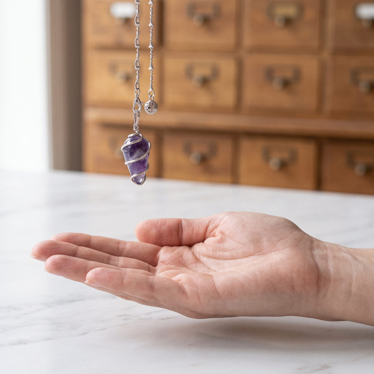 Das Amethyst-Spiralpendel hängt ruhig an seiner silberfarbenen Kette über einer offenen Handfläche
