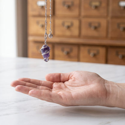 Das Amethyst-Spiralpendel hängt ruhig an seiner silberfarbenen Kette über einer offenen Handfläche