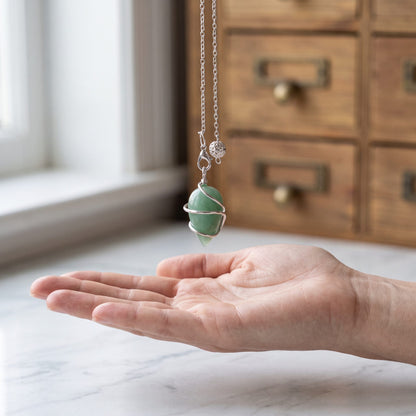 Das Aventurin-Spiralpendel hängt ruhig an seiner silberfarbenen Kette über einer offenen Handfläche