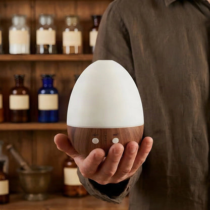Hand hält den 15,8 cm hohen Aroma Diffuser Oval Weiß vor einem Apothekerregal