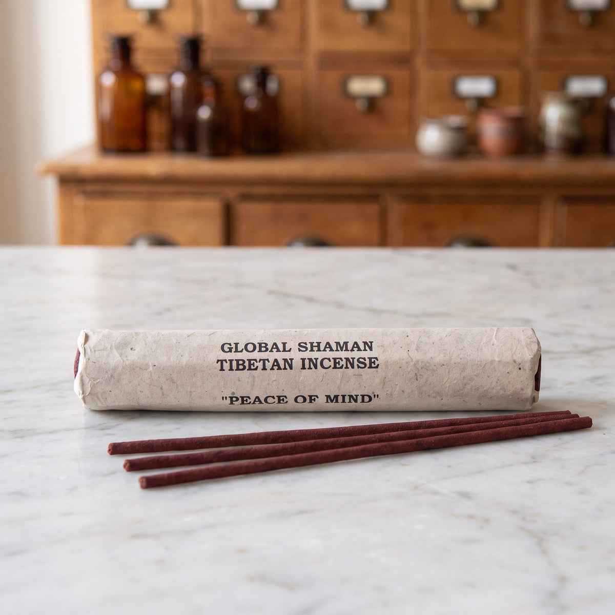 Tibetische Räucherstäbchen Frieden des Geistes (Peace of Mind): Papierrolle mit Aufdruck Global Shaman Tibetan Incense auf einer Marmortheke, davor drei dunkelrote Stäbchen