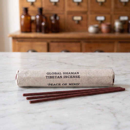 Tibetische Räucherstäbchen Frieden des Geistes (Peace of Mind): Papierrolle mit Aufdruck Global Shaman Tibetan Incense auf einer Marmortheke, davor drei dunkelrote Stäbchen