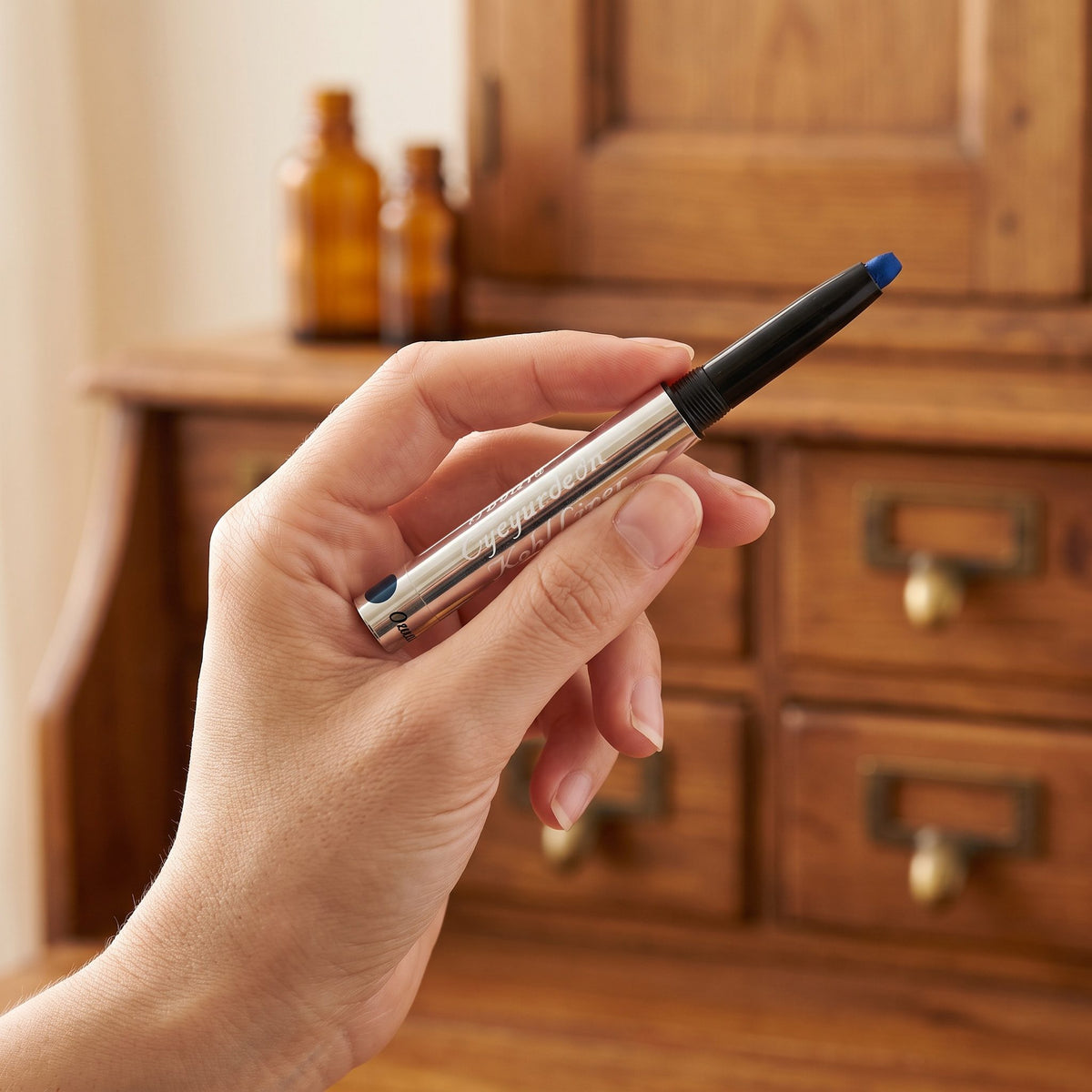 Hand hält einen Kajal-Drehstift mit blauer Mine vor einem Holzschrank