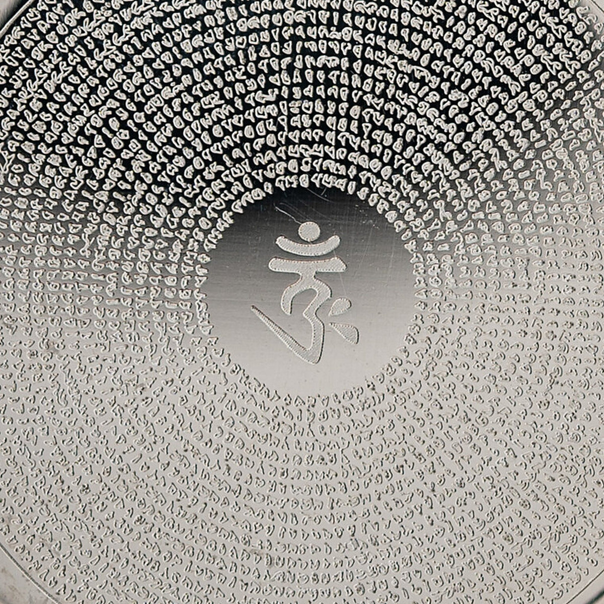 Nahaufnahme des OM im glatten Mittelfeld und der Mantra-Gravur in feinen Kreisen auf silberfarbenem Edelstahl