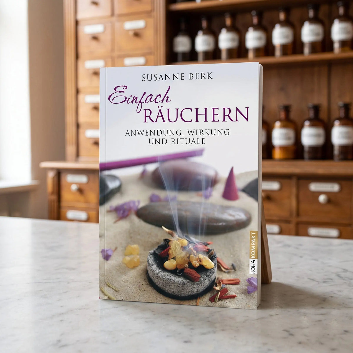 Das Buch Einfach Räuchern von Susanne Berk steht auf der Marmortheke einer hellen Apotheke