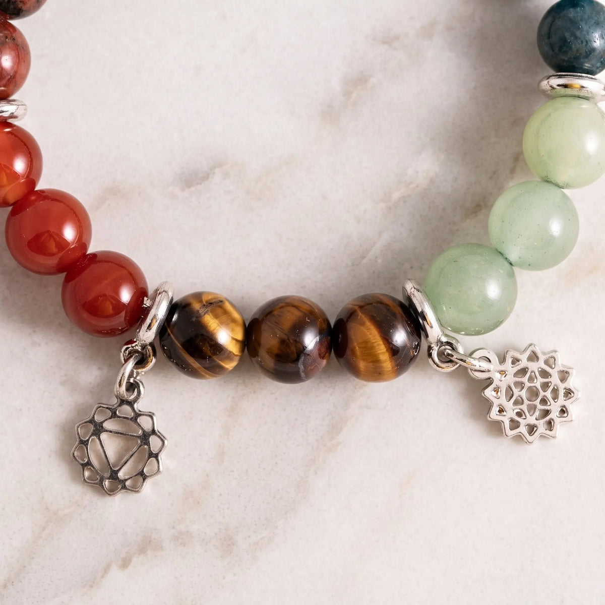 Detail des Chakra-Armbands: roter Onyx, Tigerauge und grüner Aventurin mit zwei Chakra-Anhängern auf Marmor