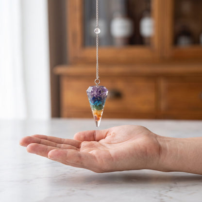 Das Chakra-Pendel hängt ruhig an seiner silberfarbenen Kette über einer offenen Handfläche