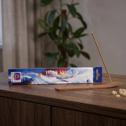 Weihrauch Räucherstäbchen Blue Line: glimmendes Räucherstäbchen mit feinem Rauch im Holzhalter, dahinter die Packung, auf einem Sideboard am Abend