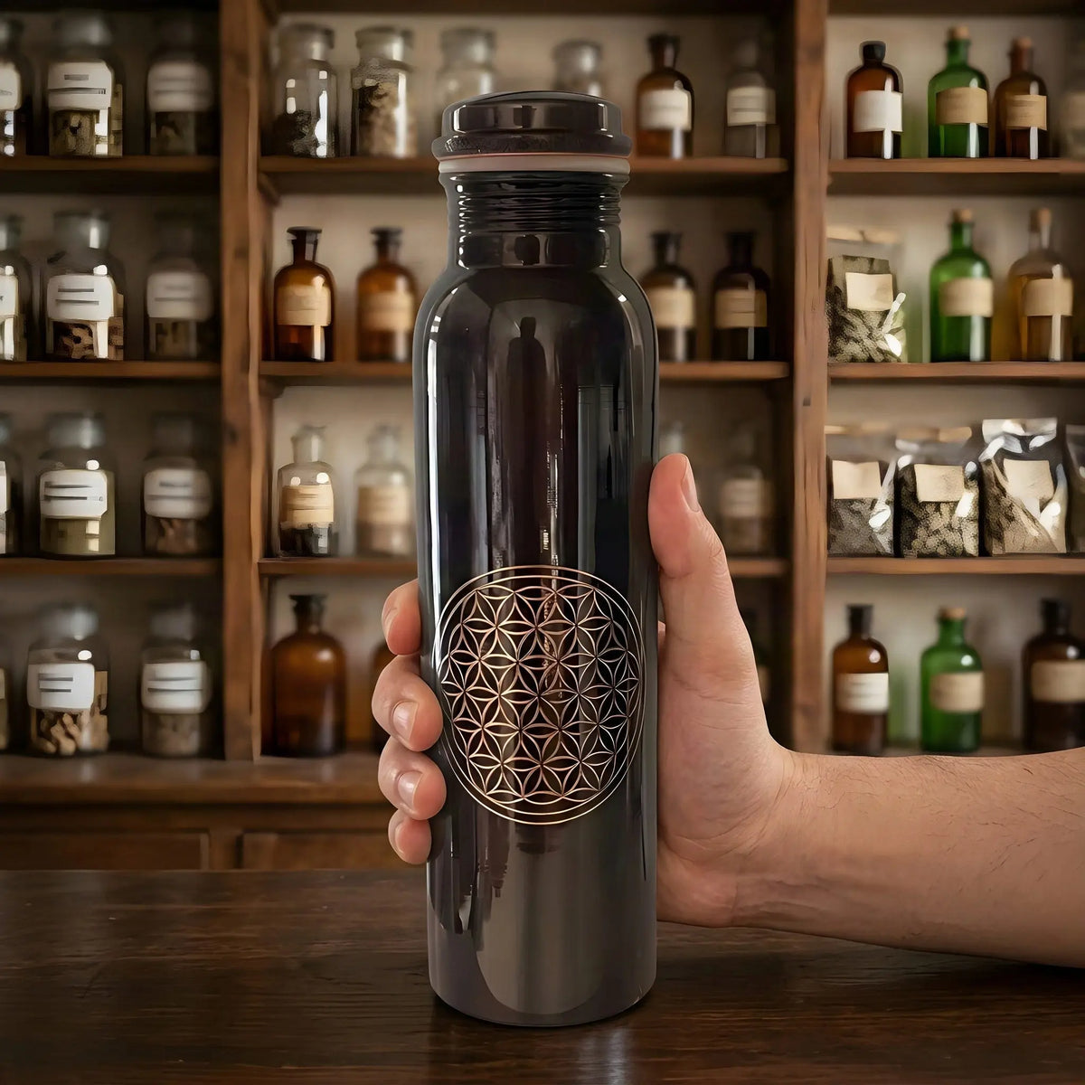 Hand hält die antik-dunkle Kupfer-Trinkflasche mit Blume des Lebens vor einem Apothekerschrank