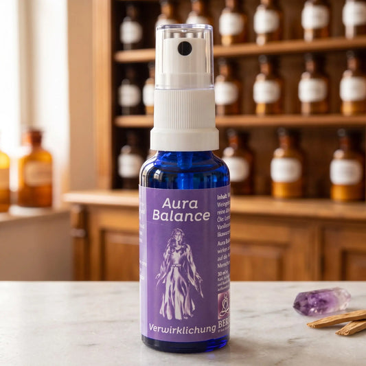 Energiespray Verwirklichung (Aura Balance): blaue Sprühflasche mit violettem Etikett auf Marmortheke vor Apothekerschrank, daneben ein Amethyst und Sandelholzspäne – Spirit of Gaia