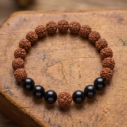 Draufsicht auf das Rudraksha Armband mit Turmalin auf altem Holz: zwei Gruppen aus je drei schwarzen Turmalinperlen zwischen Rudraksha-Samen