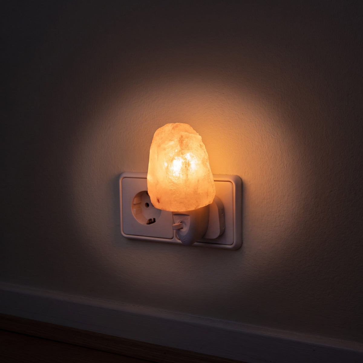 Das Salzkristall-Nachtlicht Natur in der Steckdose eines dunklen Flurs, das Licht bildet einen weichen Kreis auf der Wand