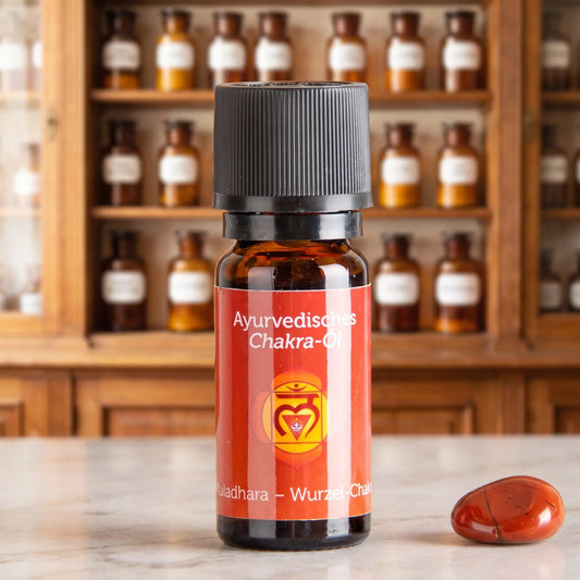 Ayurvedisches Chakra-Öl Muladhara (Wurzel-Chakra): 10-ml-Fläschchen aus Braunglas auf Marmortheke vor Apothekerschrank, daneben roter Jaspis – Spirit of Gaia