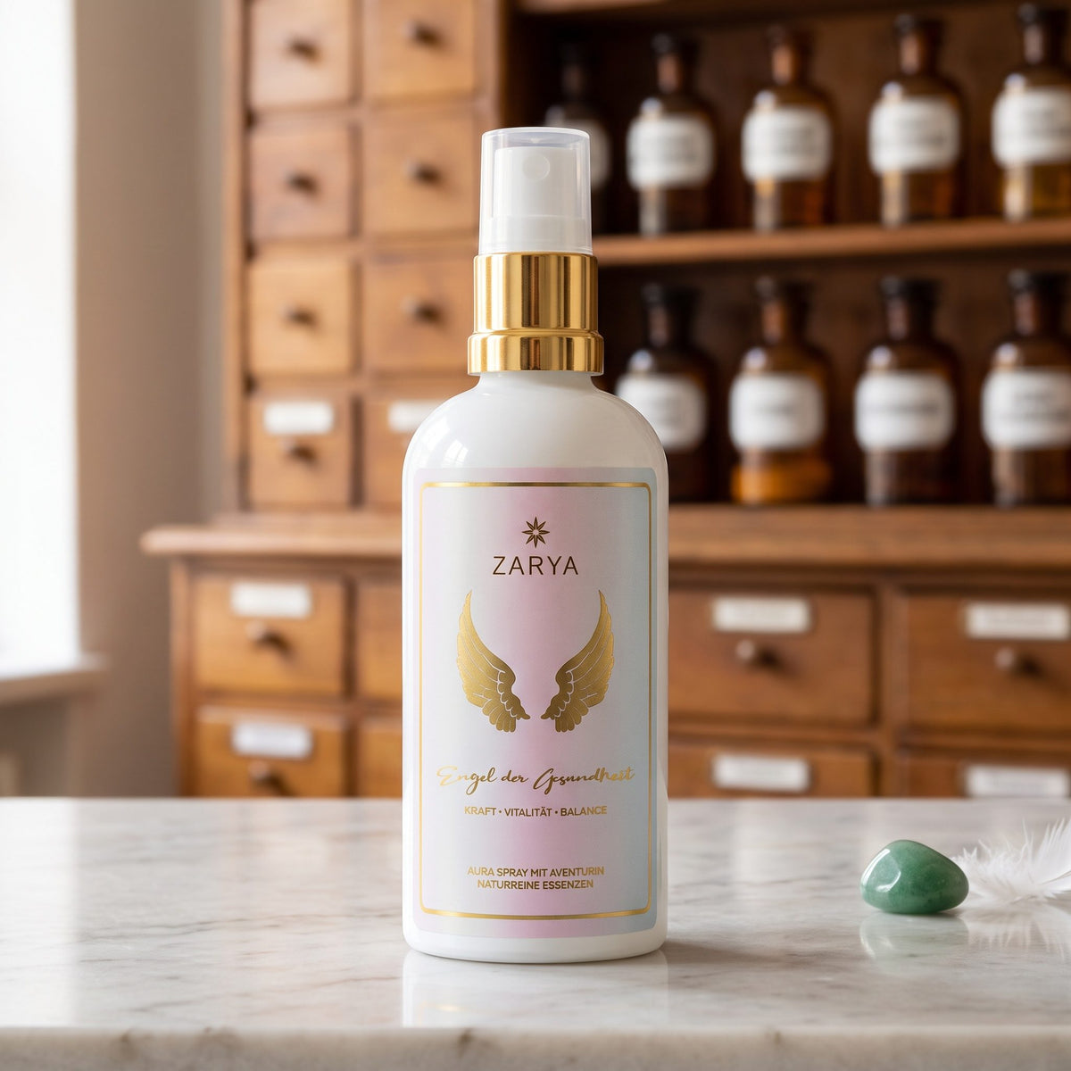 Engel der Gesundheit Aura Spray von Zarya: weiße Flasche mit goldenem Pumpring und goldenen Flügeln auf dem Etikett, auf der Marmortheke einer Apotheke, daneben ein grüner Aventurin und eine weiße Feder