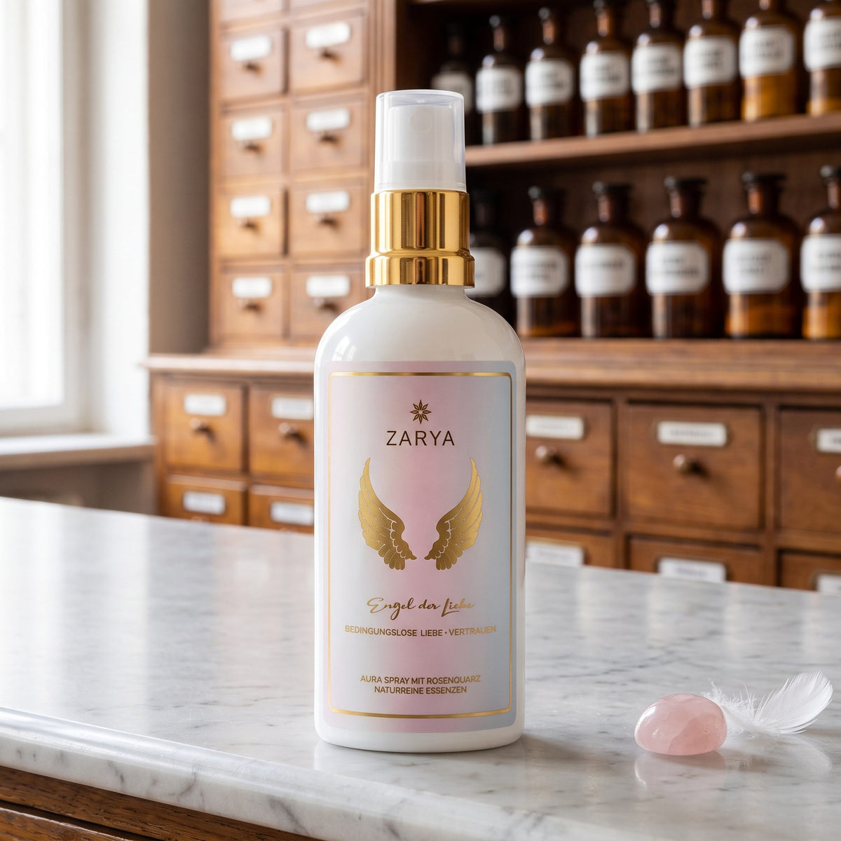Engel der Liebe Aura Spray von Zarya: weiße Flasche mit goldenem Pumpring und goldenen Flügeln auf dem Etikett, auf der Marmortheke einer Apotheke, daneben ein rosa Rosenquarz und eine weiße Feder